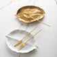 Belo Inox TWO cutlery in gold finish displayed over white and gold leaf-shaped dishes on a marble background