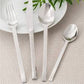 Silver cutlery set on a textured surface with a white plate and green leaves.