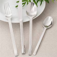 Silver cutlery set on a textured surface with a white plate and green leaves.