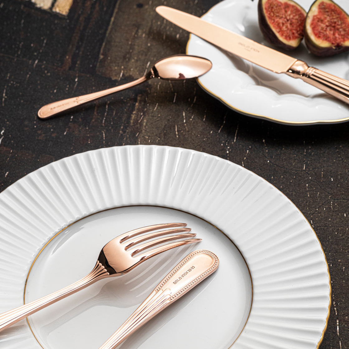 Belo Inox Alma cutlery in rose gold plated finish arranged on white ceramic plates in an elegant table setting with figs