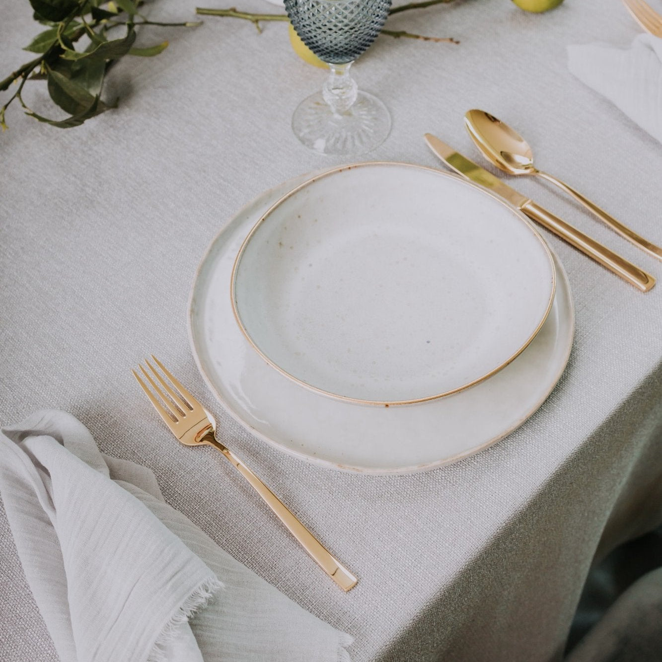 Belo Inox Belo 12 gold cutlery placed beside ceramic plates and blue glassware on a minimalist table