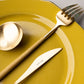 Belo Inox NEO Mustard cutlery set in brushed gold finish on a yellow plate – modern Portuguese stainless steel flatware