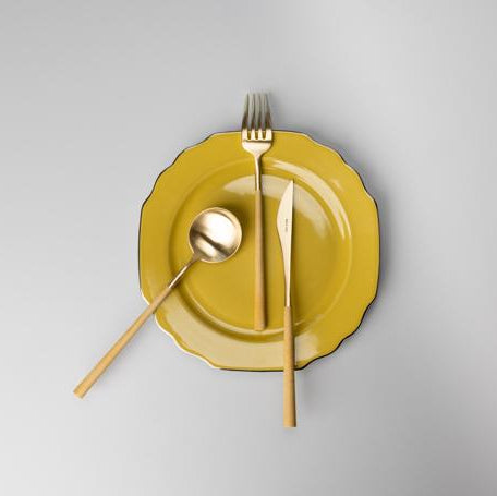 Belo Inox NEO Mustard cutlery set in brushed gold on a yellow ceramic plate, minimal lifestyle photo
