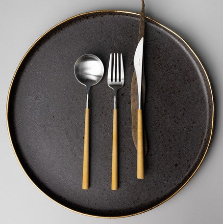 Belo Inox NEO Mustard cutlery set in brushed stainless steel with mustard resin handles, displayed on a dark ceramic plate.