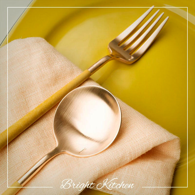 Belo Inox Neo Mustard Gold cutlery set displayed on yellow plate and linen napkin, modern stainless steel design made in Portugal.