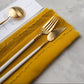 Belo Inox Neo White Gold fish knife and fork resting on a mustard linen napkin, showcasing the gold matte finish and white resin handles.

