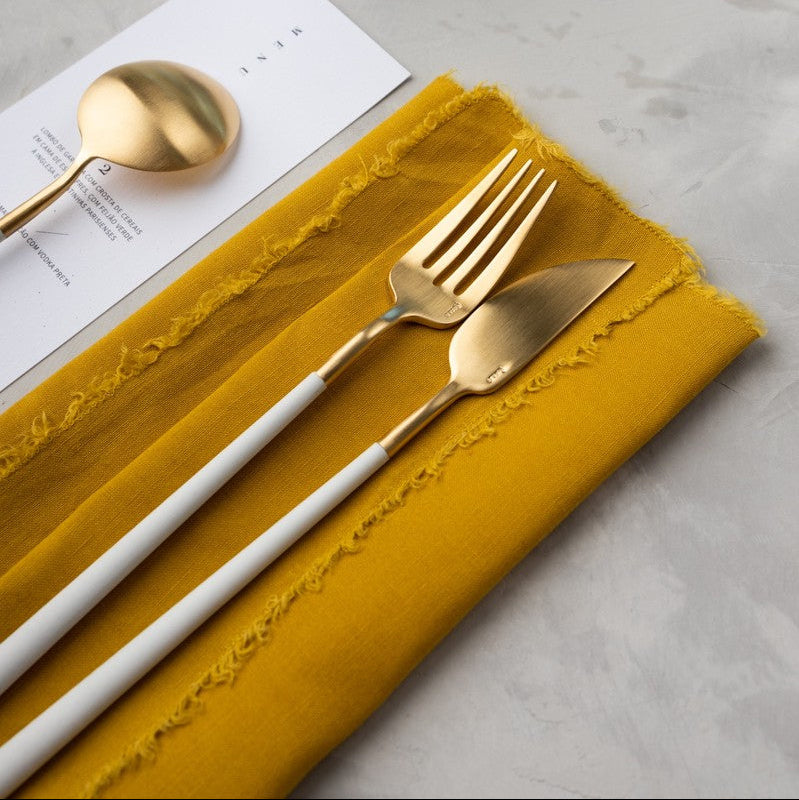 Belo Inox Neo White Gold fish knife and fork resting on a mustard linen napkin, showcasing the gold matte finish and white resin handles.
