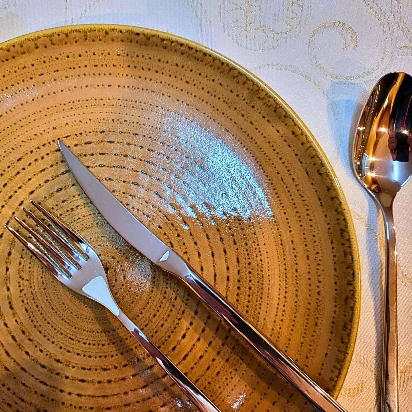 Belo Inox Nomo polished stainless steel fork and knife on a textured beige ceramic plate, fine dining table setting
