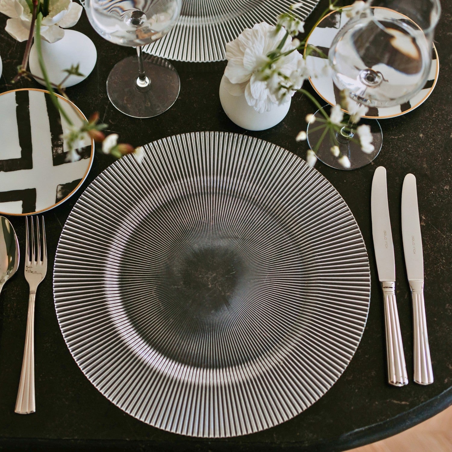 Refined table setting featuring Belo Inox Príncipe cutlery arranged beside a black-and-white patterned plate on a dark elegant surface