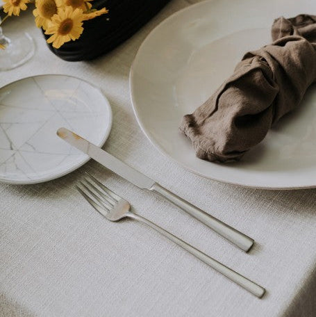 Belo Inox Touch matte cutlery — table knife and fork styled on an elegant neutral table setting with yellow floral centerpiece