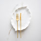 Belo Inox TWO gold matte cutlery set displayed on a white leaf-shaped plate over a marble surface.
