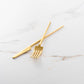 Two Belo Inox TWO forks in titanium matte gold finish displayed on a white marble surface