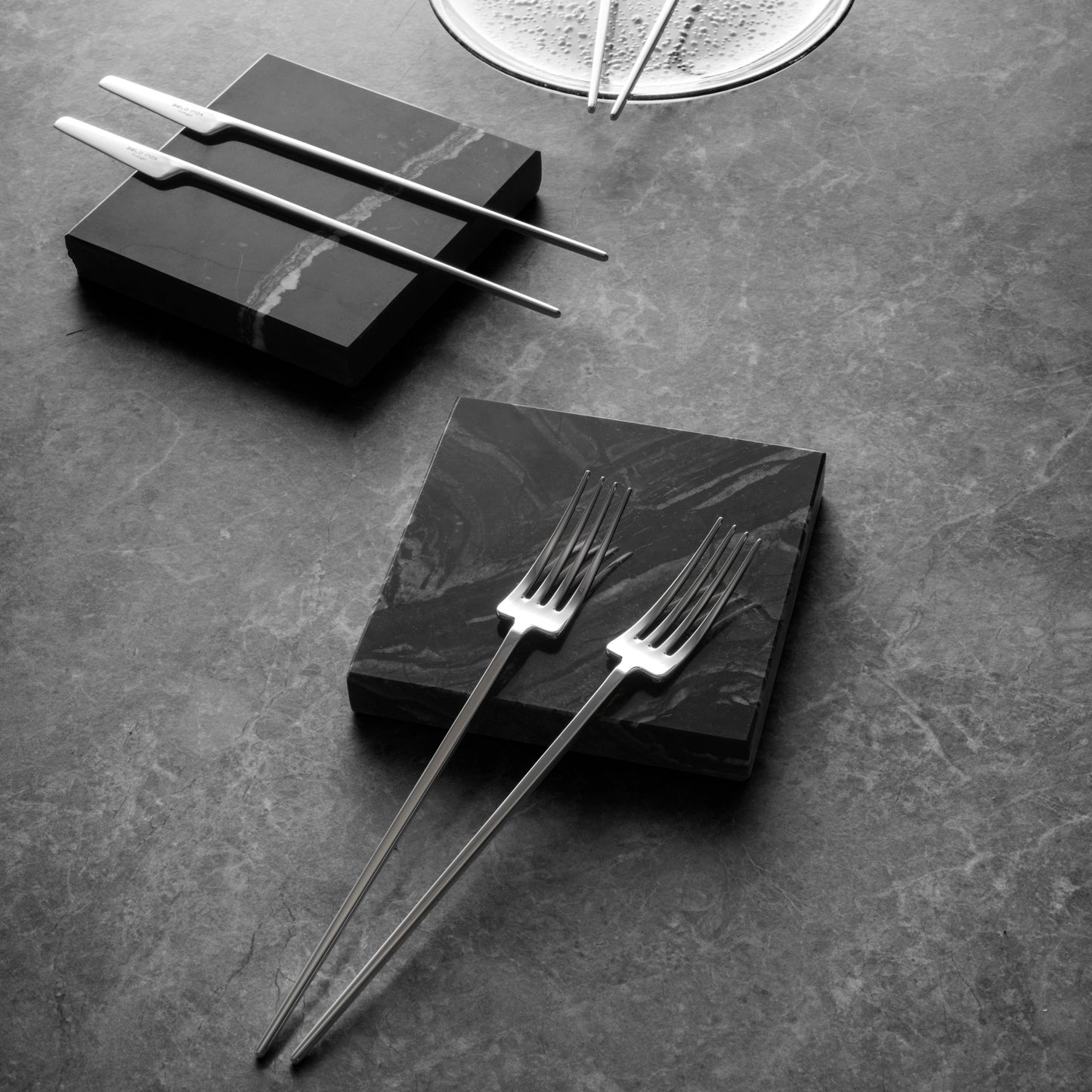 Belo Inox TWO Titanium Mirror cutlery set displayed on dark stone surface, featuring modern knife and forks in a luxurious ambience
