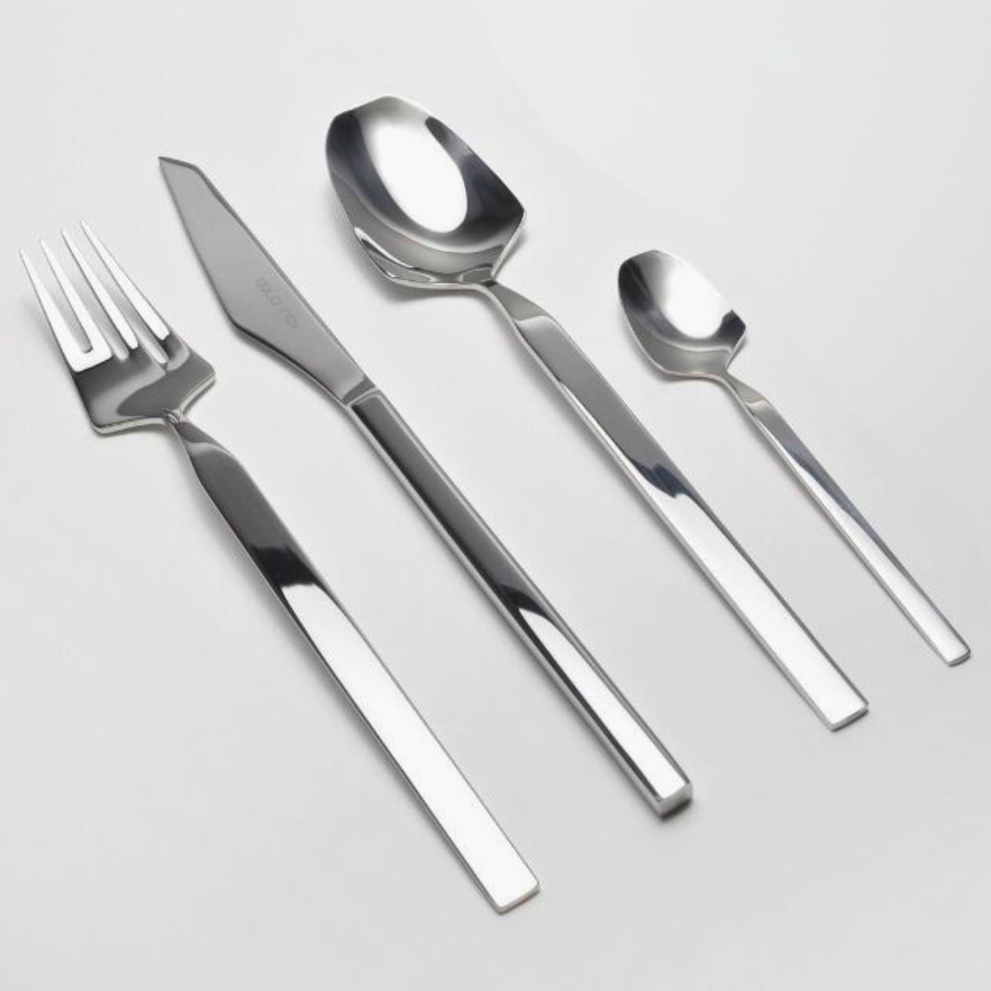 Belo Inox Vertice polished stainless steel flatware set featuring dinner knife, dinner fork, tablespoon and teaspoon on a light background