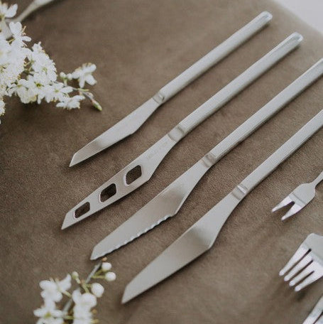 Belo Inox Vertice collection knives — table knife, steak knife, cheese knife and dessert knife — displayed in a soft floral setting