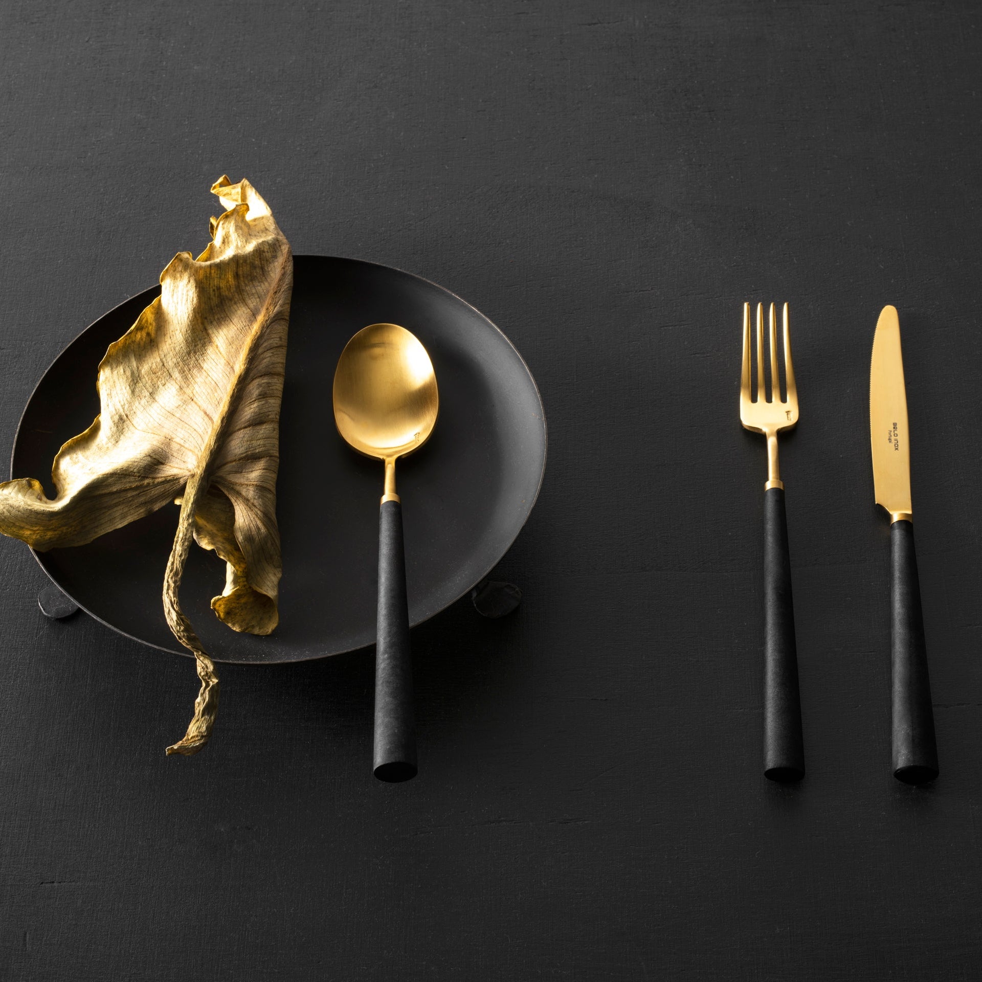 Belo Inox Yume black and gold cutlery styled on a dark table setting with decorative elements
