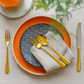 Cutipol Alcantara gold flatware set on a styled table with patterned plates and linen napkin.