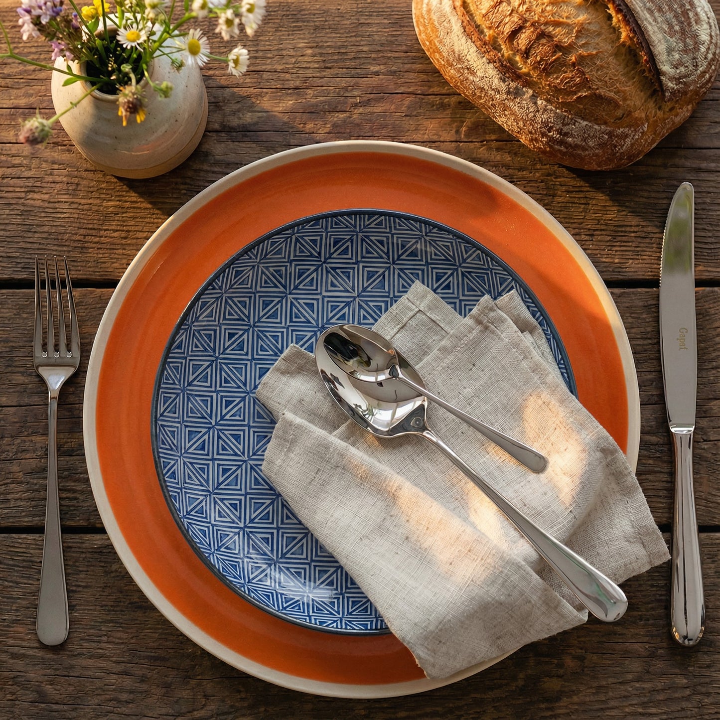 Cutipol Alcântara stainless steel cutlery set on a rustic table with ceramic plates and linen napkin