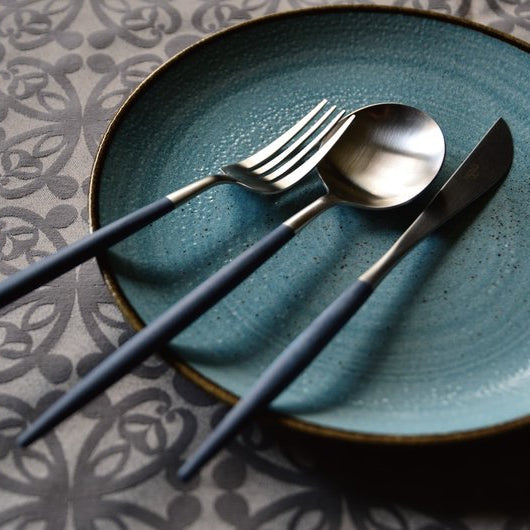 Cutipol Goa Blue flatware set placed on a blue ceramic plate over a patterned tablecloth