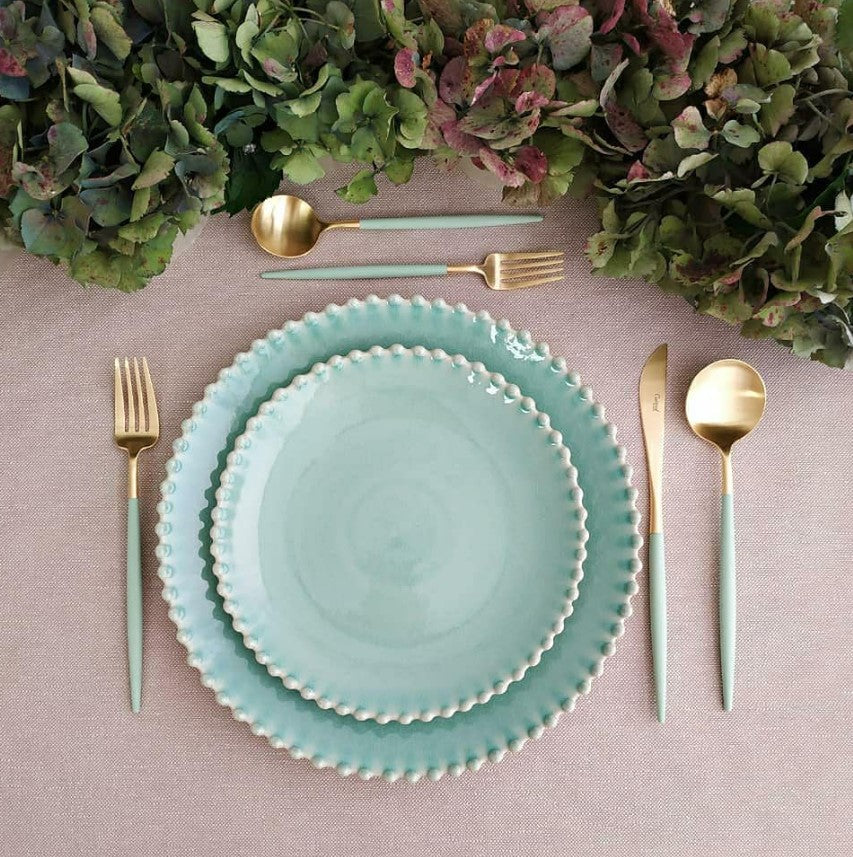 Cutipol GOA Celadon Gold cutlery arranged with aqua ceramic plates and hydrangeas on a pink tablecloth
