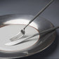 Elegant Cutipol Goa Grey knife and fork set on a modern white and silver plate, showcasing minimalist design