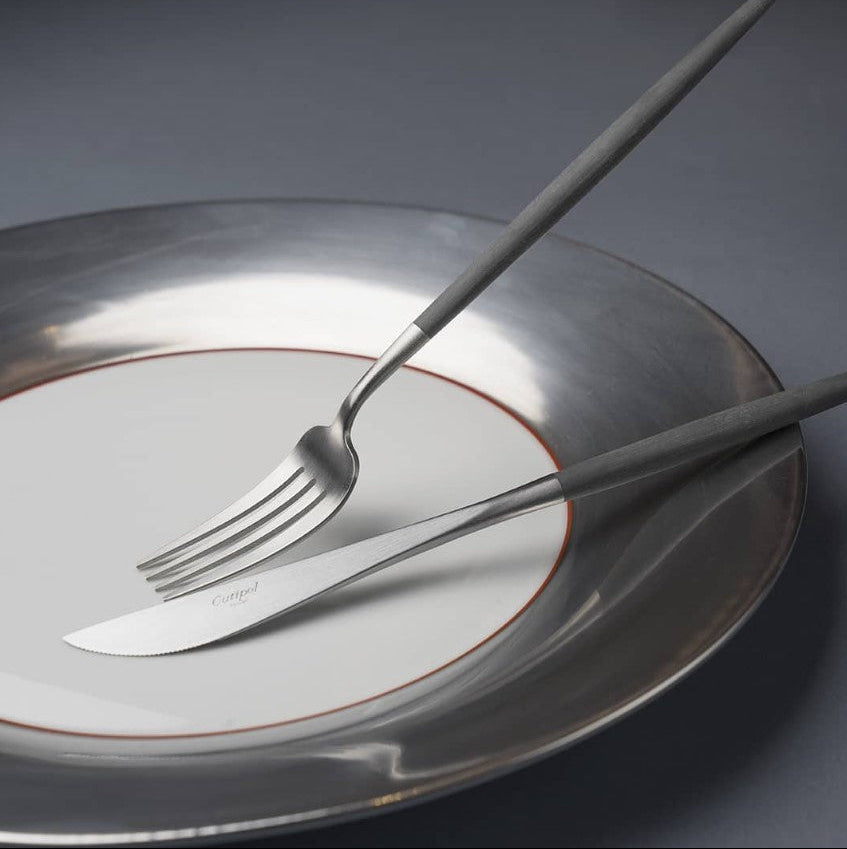 Elegant Cutipol Goa Grey knife and fork set on a modern white and silver plate, showcasing minimalist design