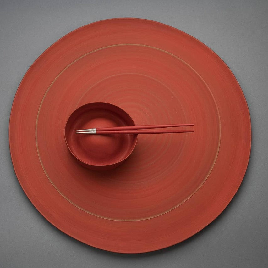 Red Cutipol Goa chopsticks resting on a matching red bowl and plate set against a gray background.