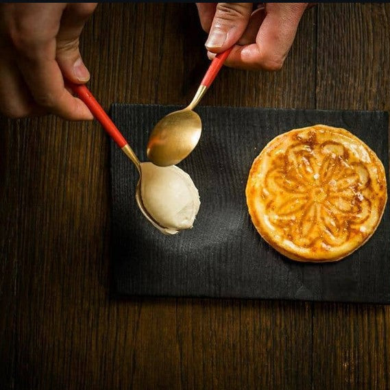 Cutipol GOA Red Gold spoons serving ice cream next to a baked dessert on a dark wooden table