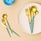 Cutipol GOA Turquoise Gold cutlery arranged on a white plate over a beige background, with a blue glass beside it