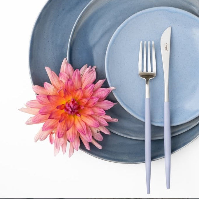 Cutipol GOA Violet cutlery placed on layered blue ceramic plates with a pink and orange flower