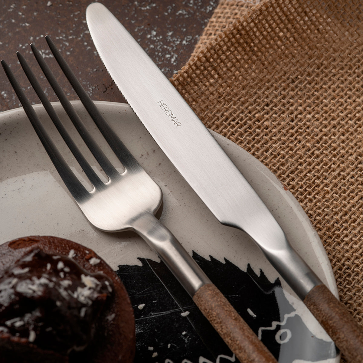 Close-up of Herdmar NOHC cutlery set in stainless steel with textured brown handles and elegant table setting.