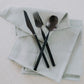 Belo Inox Vértice black PVD brushed cutlery set displayed on soft neutral napkins